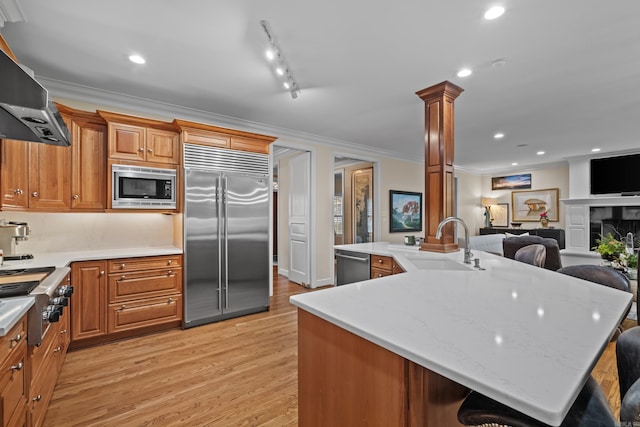 kitchen with sink, a spacious island, built in appliances, ventilation hood, and a kitchen bar