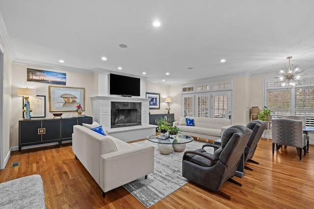 living room featuring an inviting chandelier, hardwood / wood-style floors, ornamental molding, and a tile fireplace