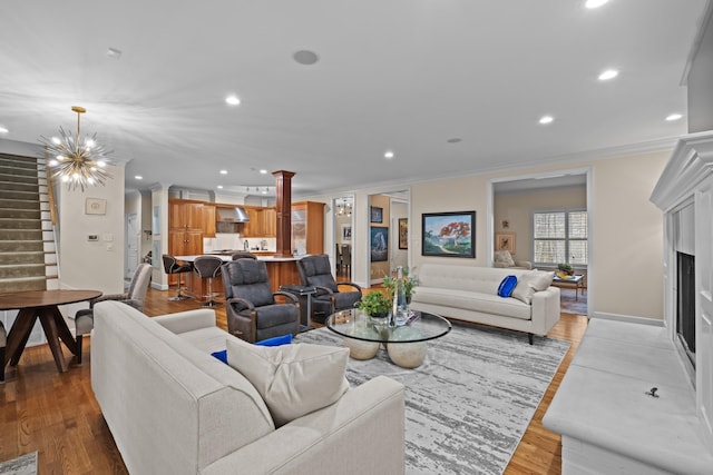 living room with an inviting chandelier, crown molding, light hardwood / wood-style floors, and ornate columns