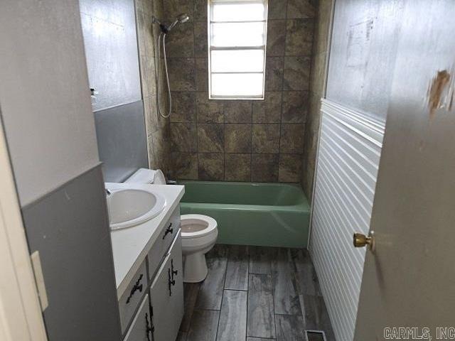 full bathroom featuring vanity, hardwood / wood-style floors, tiled shower / bath combo, and toilet