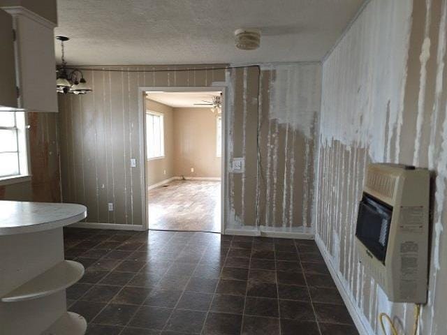 unfurnished living room with heating unit, ceiling fan with notable chandelier, and wood walls