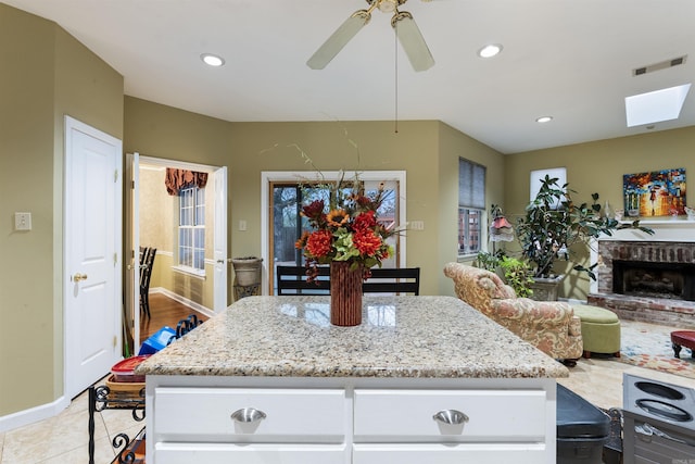 kitchen with light tile patterned floors, ceiling fan, a fireplace, light stone countertops, and white cabinets