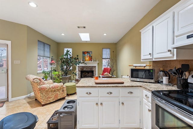 kitchen with white cabinetry, a brick fireplace, light tile patterned floors, stainless steel appliances, and decorative backsplash