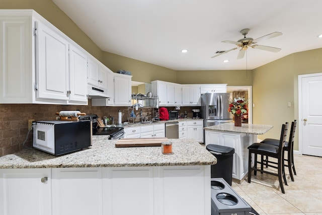 kitchen featuring a breakfast bar area, white cabinets, kitchen peninsula, stainless steel appliances, and light stone countertops