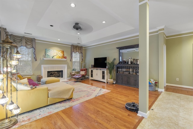 living room featuring hardwood / wood-style flooring, ornamental molding, a fireplace, and a raised ceiling