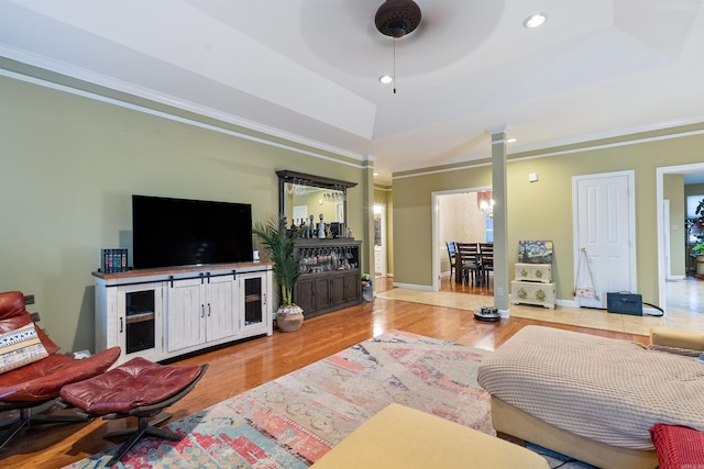 living room featuring hardwood / wood-style floors, ornamental molding, a raised ceiling, and ornate columns