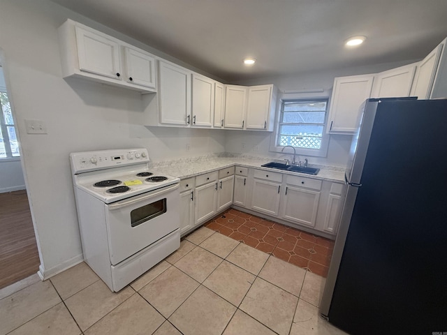 kitchen featuring sink, light tile patterned floors, stainless steel fridge, electric stove, and white cabinets