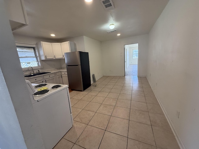 kitchen with light tile patterned flooring, stainless steel refrigerator, white cabinetry, sink, and electric stove