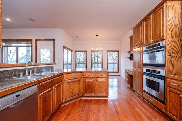 kitchen featuring decorative light fixtures, sink, stainless steel appliances, crown molding, and light hardwood / wood-style flooring