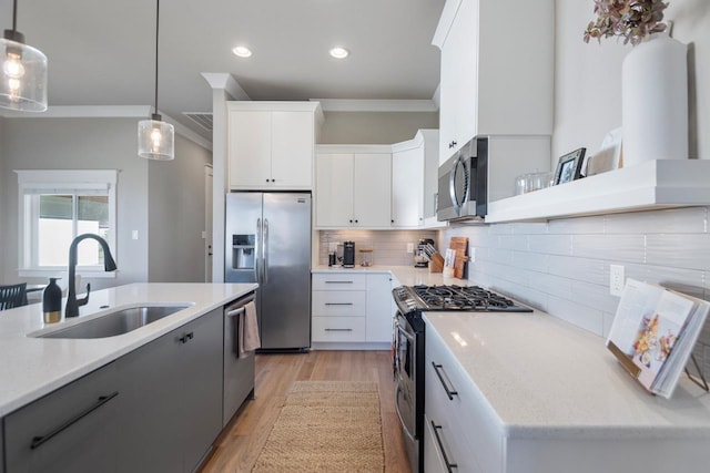 kitchen featuring sink, appliances with stainless steel finishes, hanging light fixtures, ornamental molding, and white cabinets