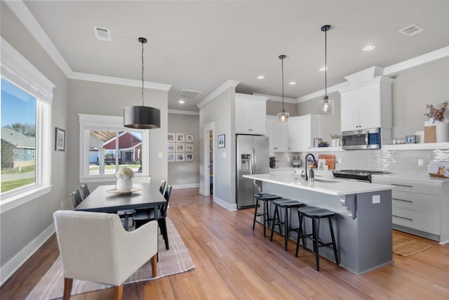 kitchen with sink, hanging light fixtures, appliances with stainless steel finishes, an island with sink, and white cabinets