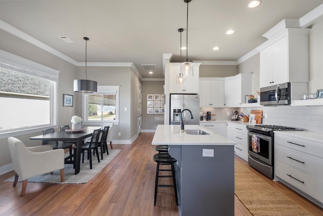 kitchen with pendant lighting, sink, a kitchen island with sink, stainless steel appliances, and white cabinets