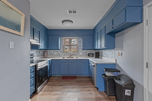 kitchen with blue cabinetry, appliances with stainless steel finishes, light hardwood / wood-style floors, and decorative backsplash