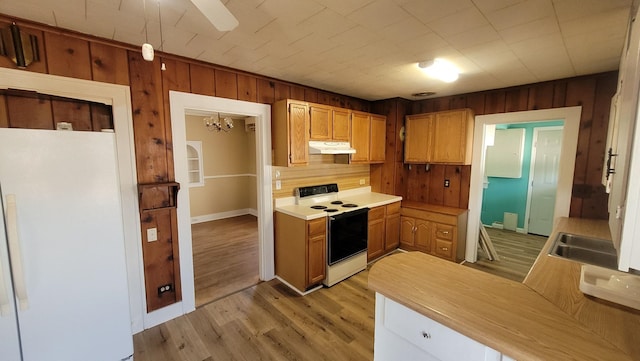 kitchen with white appliances, light wood finished floors, wooden walls, light countertops, and under cabinet range hood