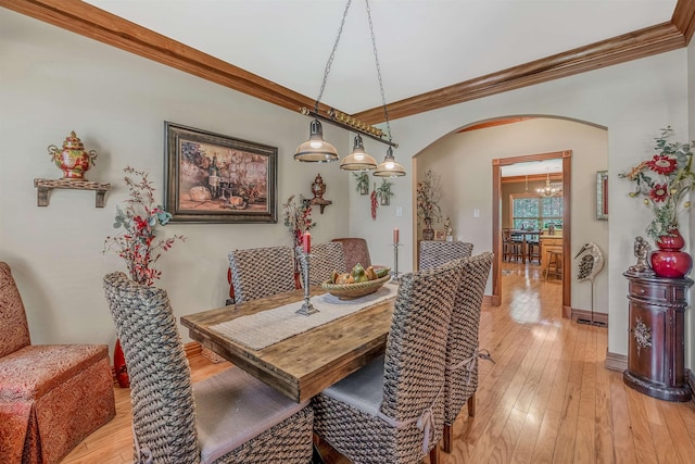 dining room with arched walkways, light wood finished floors, ornamental molding, and baseboards