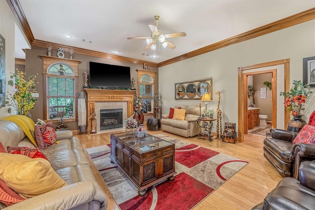 living room featuring a high end fireplace, light hardwood / wood-style flooring, ornamental molding, and ceiling fan