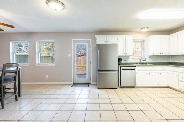 kitchen with light tile patterned floors, appliances with stainless steel finishes, tasteful backsplash, a wealth of natural light, and white cabinets