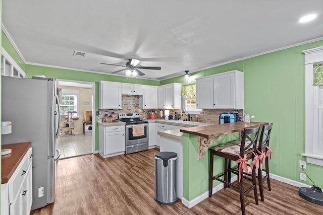 kitchen with a kitchen bar, butcher block counters, sink, white cabinetry, and appliances with stainless steel finishes