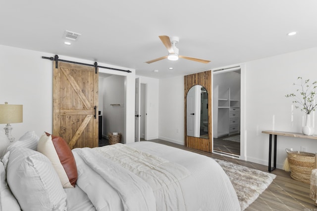 bedroom with ceiling fan, wood-type flooring, a barn door, and a closet