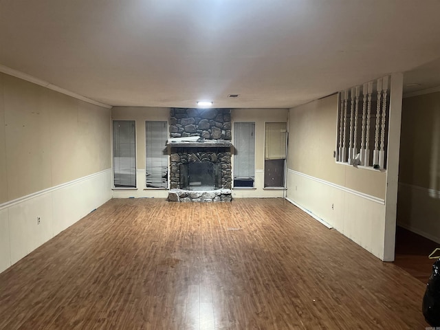 unfurnished living room with dark wood-type flooring, a stone fireplace, and crown molding