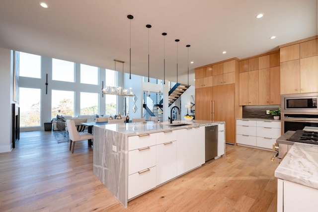 kitchen with appliances with stainless steel finishes, decorative light fixtures, sink, a large island with sink, and light brown cabinets