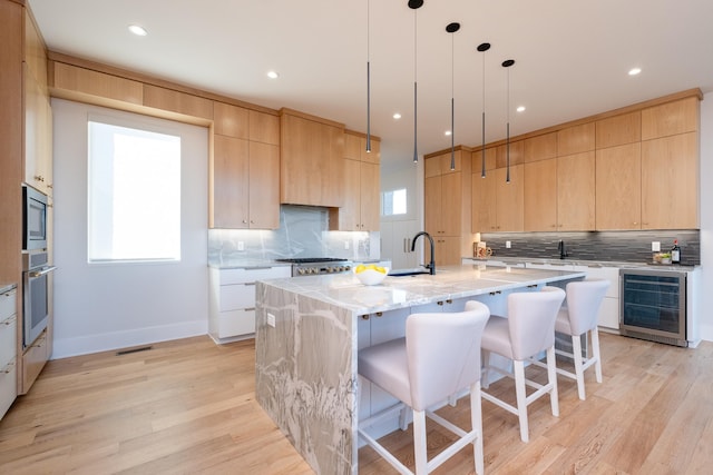 kitchen featuring a kitchen island with sink, light brown cabinetry, wine cooler, and light stone countertops