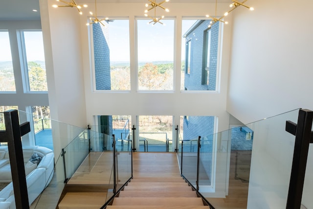 stairs with a towering ceiling, wood-type flooring, and a notable chandelier