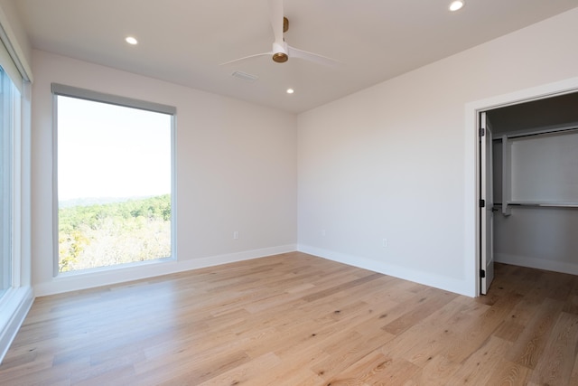 unfurnished bedroom featuring ceiling fan, light hardwood / wood-style floors, and a walk in closet