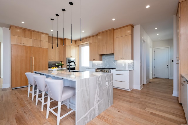 kitchen featuring stainless steel microwave, sink, a kitchen island with sink, light stone countertops, and light brown cabinets