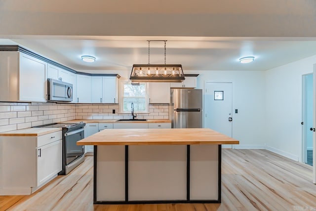 kitchen featuring pendant lighting, stainless steel appliances, butcher block counters, and sink