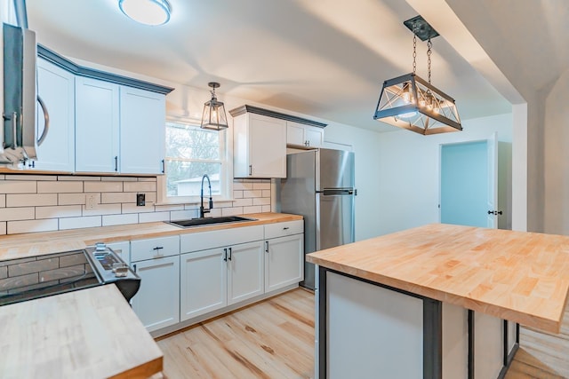 kitchen with pendant lighting, sink, white cabinetry, wood counters, and decorative backsplash