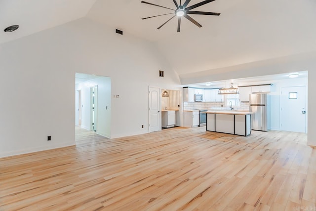 unfurnished living room featuring sink, light hardwood / wood-style flooring, and high vaulted ceiling