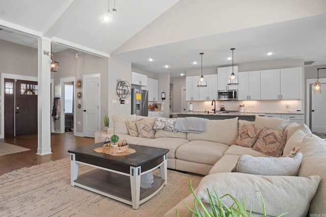 living room with sink, light hardwood / wood-style floors, high vaulted ceiling, and ornate columns