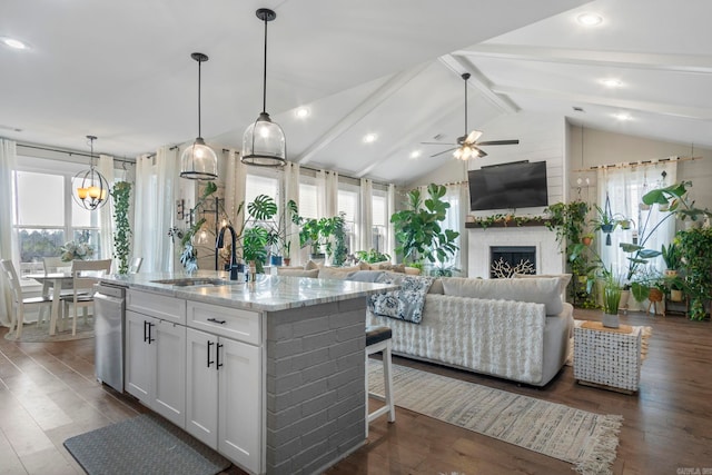 kitchen with sink, white cabinetry, hanging light fixtures, light stone countertops, and a center island with sink