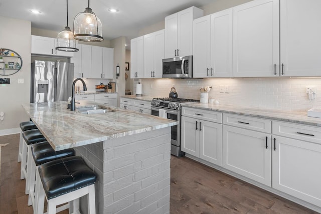 kitchen with white cabinetry, sink, stainless steel appliances, light stone countertops, and a center island with sink