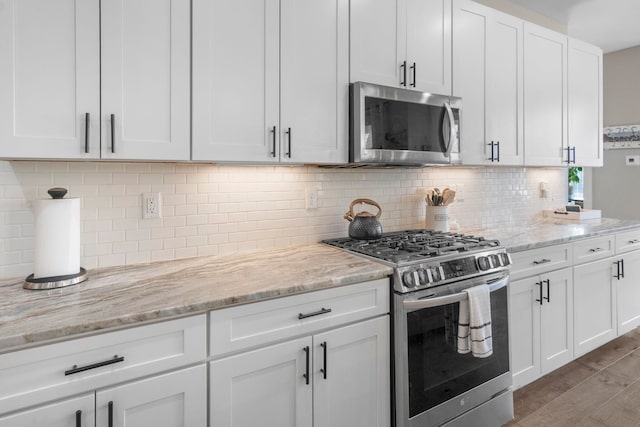 kitchen with light hardwood / wood-style flooring, appliances with stainless steel finishes, tasteful backsplash, light stone countertops, and white cabinets