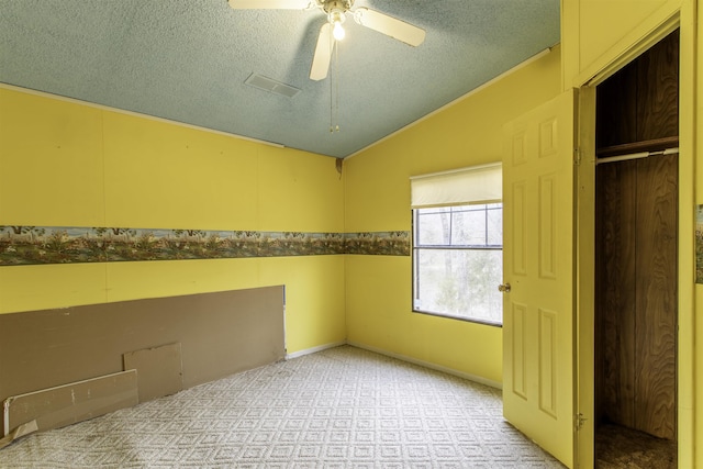 carpeted empty room featuring ceiling fan, vaulted ceiling, and a textured ceiling