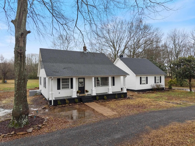 view of front of house with a shingled roof, a chimney, and a porch