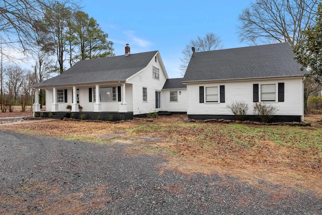 view of front of home with covered porch, roof with shingles, and a chimney