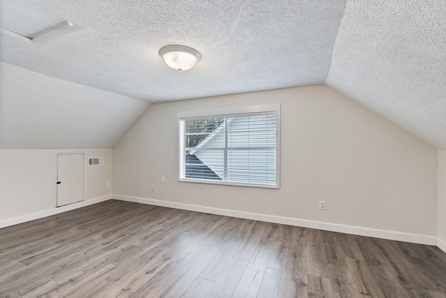 additional living space featuring lofted ceiling, wood-type flooring, and a textured ceiling