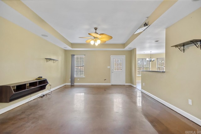 interior space featuring concrete flooring, ceiling fan with notable chandelier, and a tray ceiling