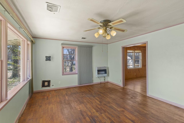 empty room with dark wood-type flooring, a wealth of natural light, and heating unit