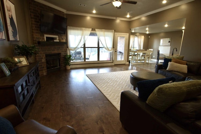 living room with ceiling fan, a brick fireplace, crown molding, and dark hardwood / wood-style flooring