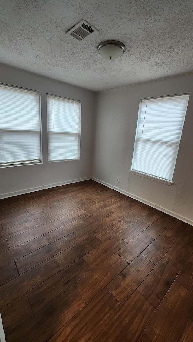 spare room with plenty of natural light, a textured ceiling, and dark wood finished floors