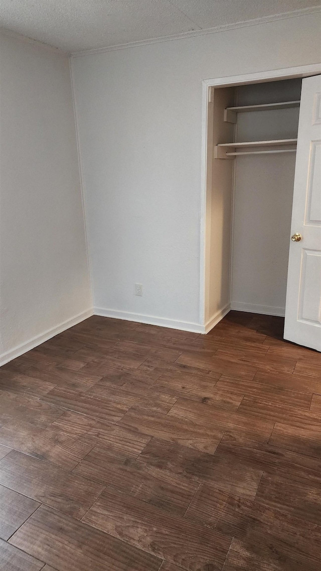 unfurnished bedroom featuring dark wood-type flooring, a textured ceiling, baseboards, and a closet