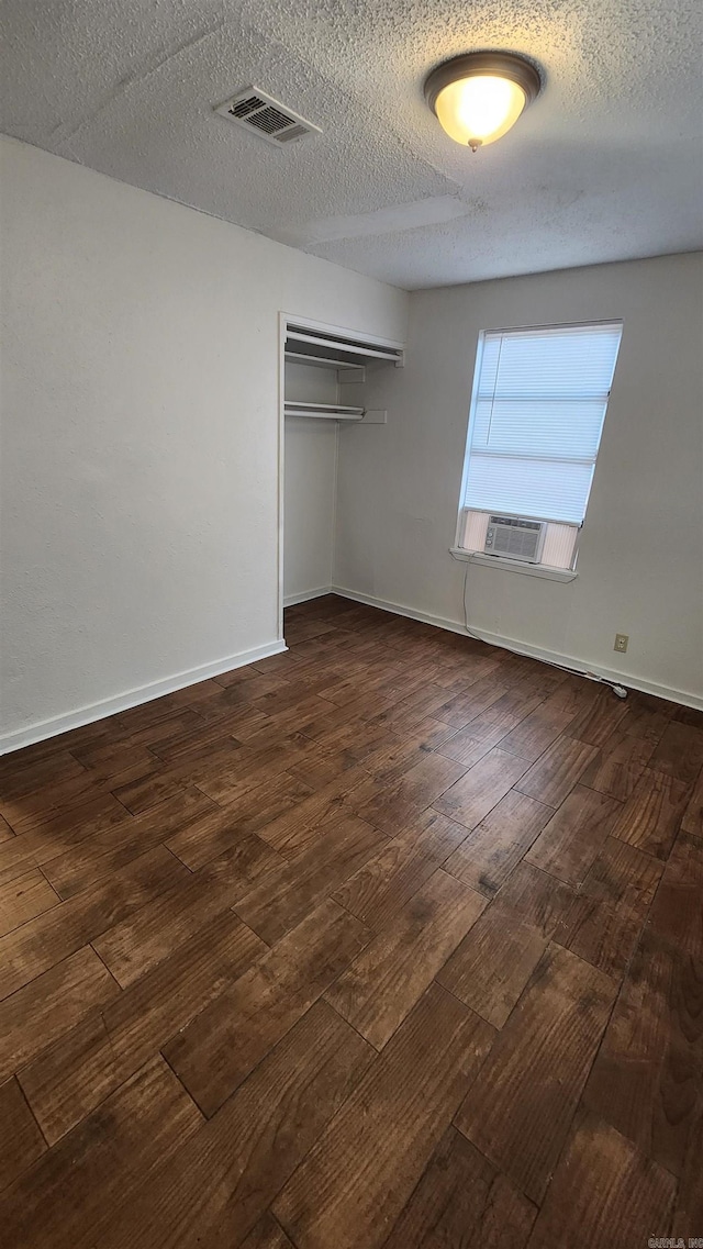 unfurnished bedroom featuring baseboards, dark wood finished floors, a textured ceiling, visible vents, and a closet