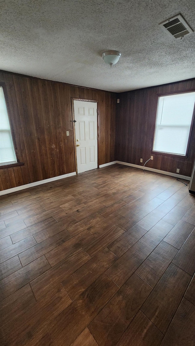 spare room with dark wood finished floors, a textured ceiling, baseboards, and visible vents