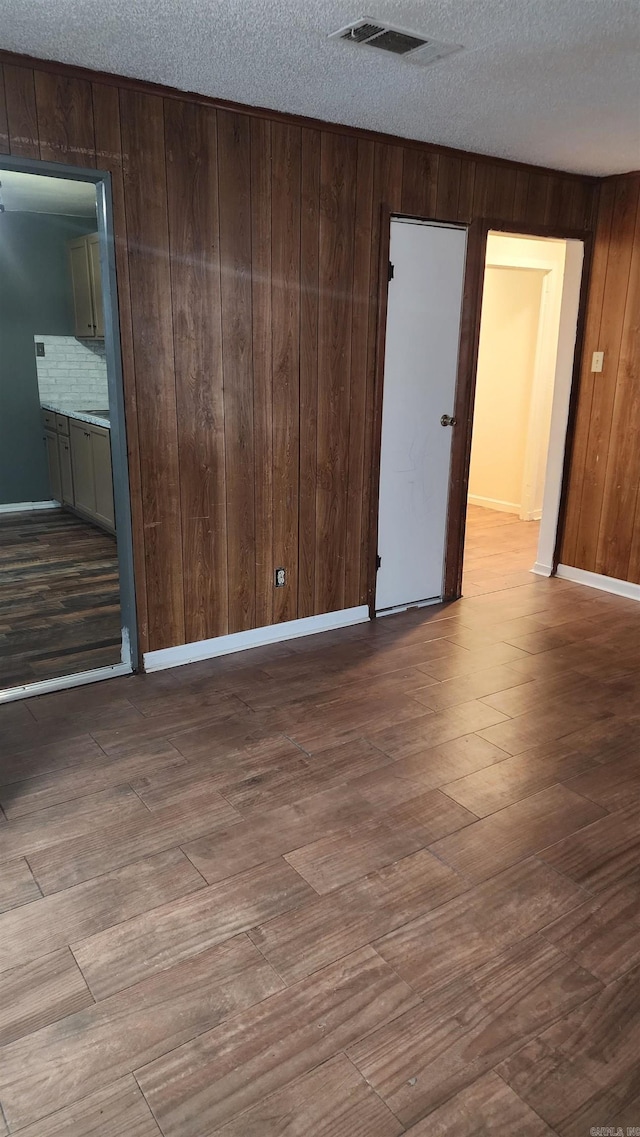 empty room featuring wooden walls, wood finished floors, a textured ceiling, baseboards, and visible vents
