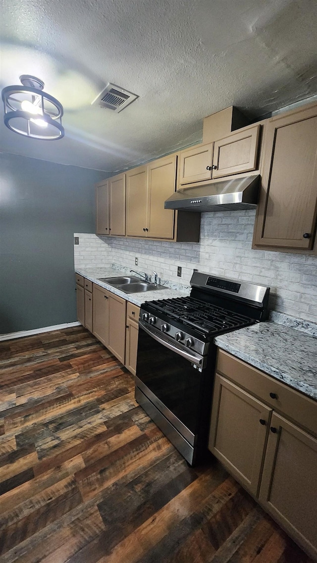 kitchen with tasteful backsplash, dark wood-style flooring, under cabinet range hood, gas stove, and a sink