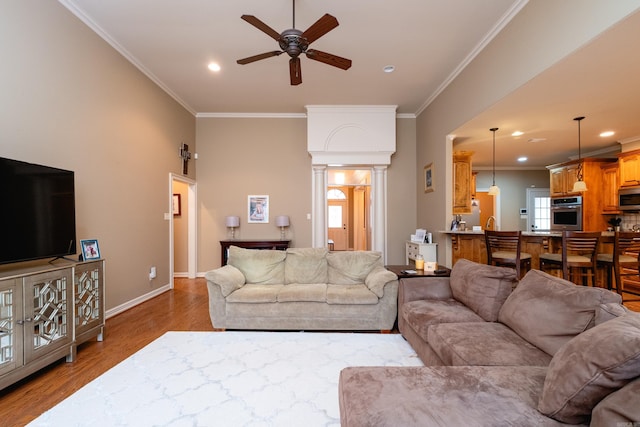 living room featuring crown molding, light hardwood / wood-style floors, ceiling fan, and ornate columns